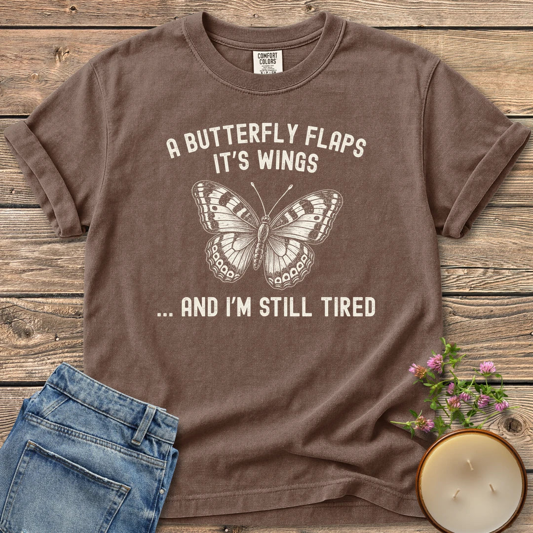 And I'm Still Tired t-shirt, a detailed butterfly between A Butterfly Flaps It's Wings and ... And I'm Still Tired, on an Espresso Comfort Colors tee