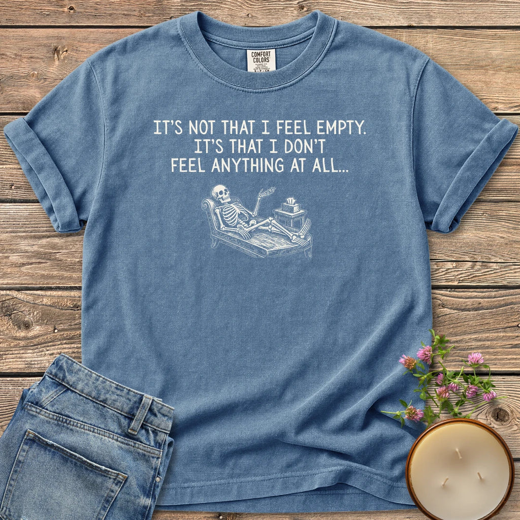 Don't Feel Anything At All t-shirt, a skeleton on a therapy couch under It's Not That I Feel Empty. It's That I Don't Feel Anything At All, on a Blue Jean Comfort Colors tee