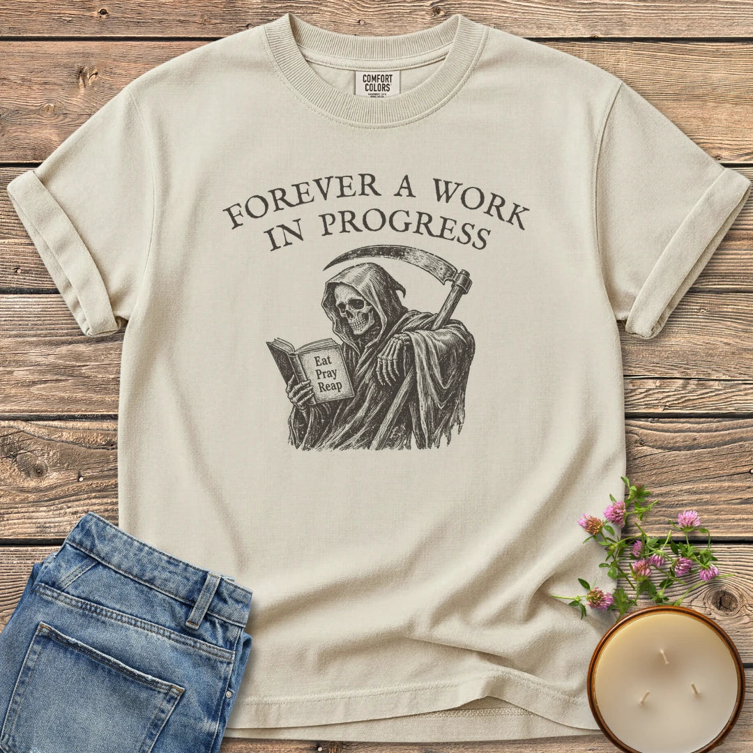 Eat Pray Reap t-shirt, a grim reaper reading a book titled Eat Pray Reap under Forever A Work In Progress, on an Ivory Comfort Colors tee