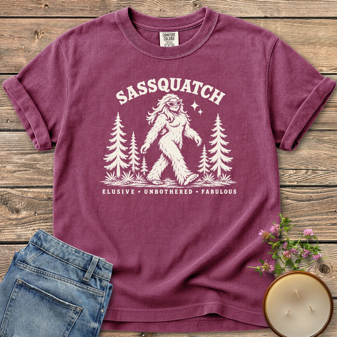 Elusive Unbothered Fabulous t-shirt, a Sassquatch in cat-eye glasses striding through pine trees above Elusive, Unbothered, Fabulous, on a Berry Comfort Colors tee