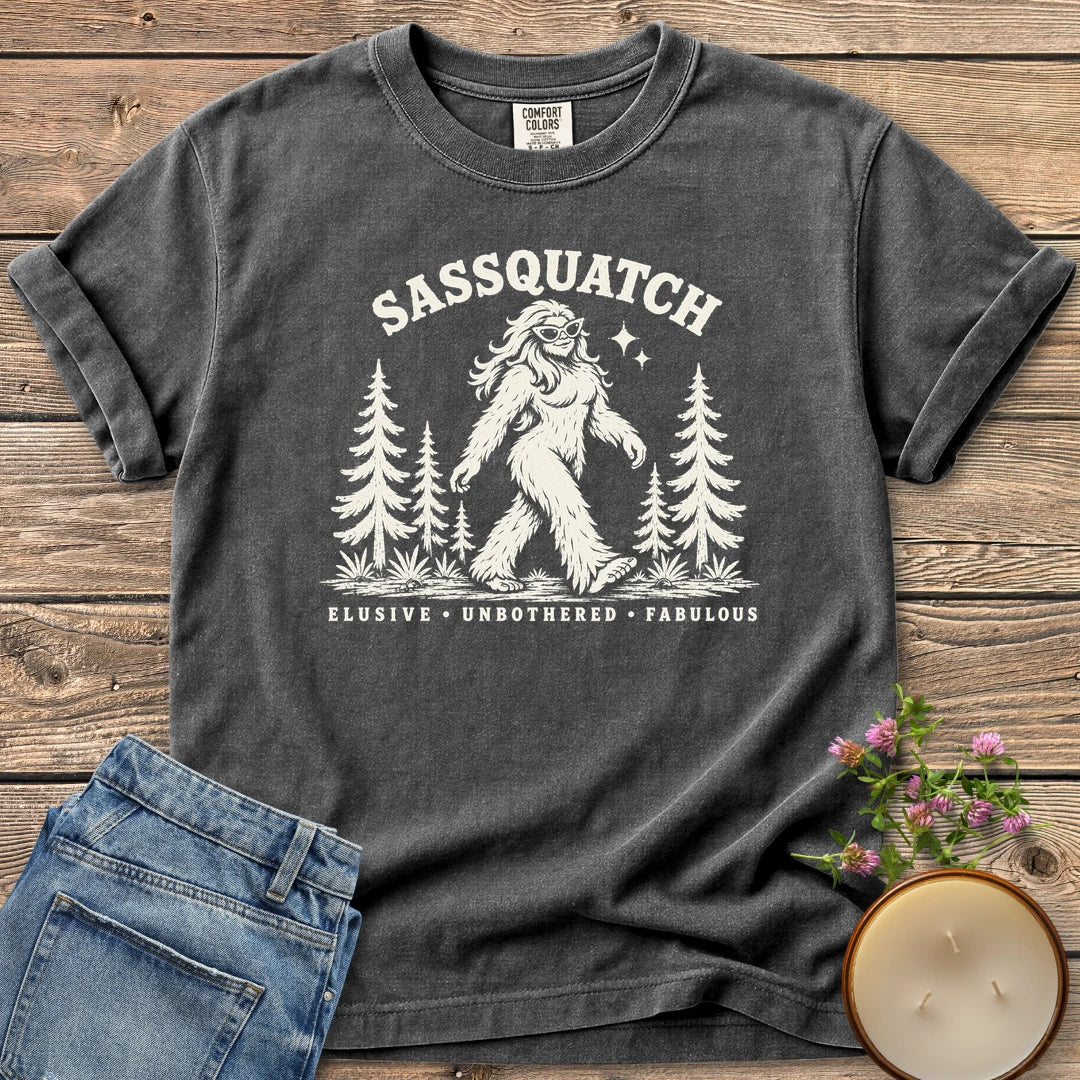 Elusive Unbothered Fabulous t-shirt, a Sassquatch in cat-eye glasses striding through pine trees above Elusive, Unbothered, Fabulous, on a Pepper Comfort Colors tee