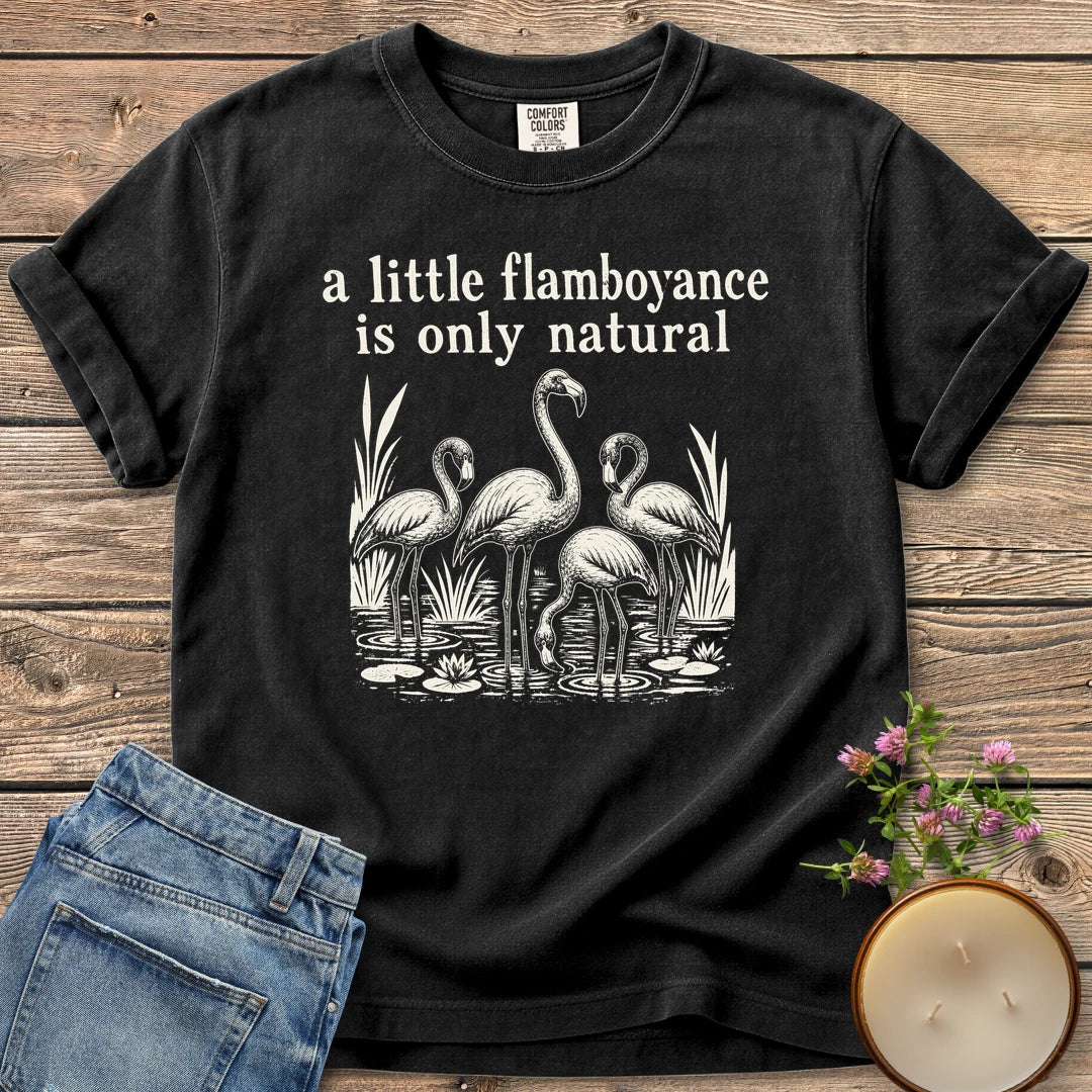 Flamboyance Is Only Natural t-shirt, a group of flamingos wading in a pond under a little flamboyance is only natural, on a Black Comfort Colors tee