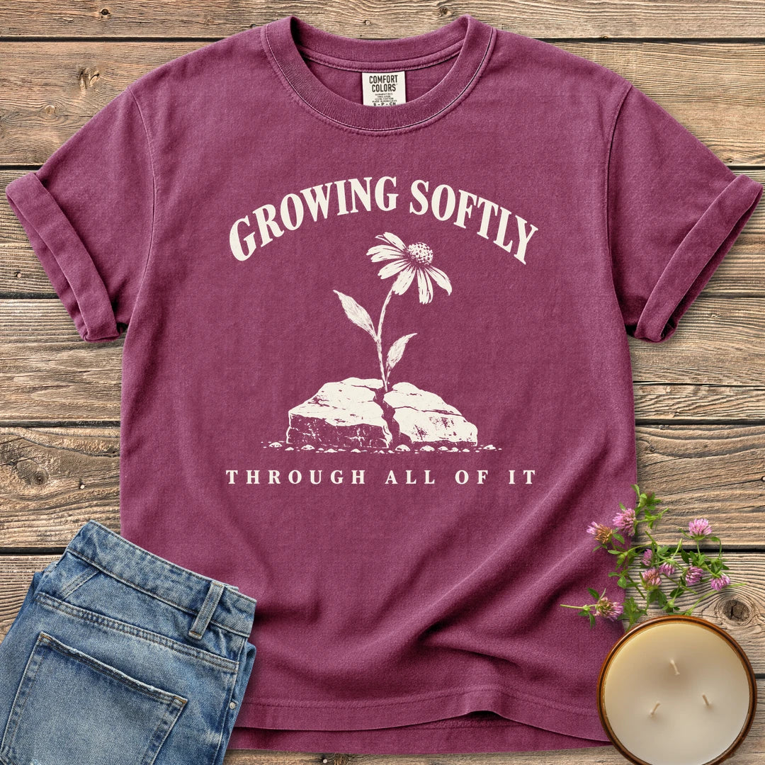 Growing Softly Through It All t-shirt, Growing Softly above a flower breaking through a cracked rock and Through All Of It, on a Berry Comfort Colors tee