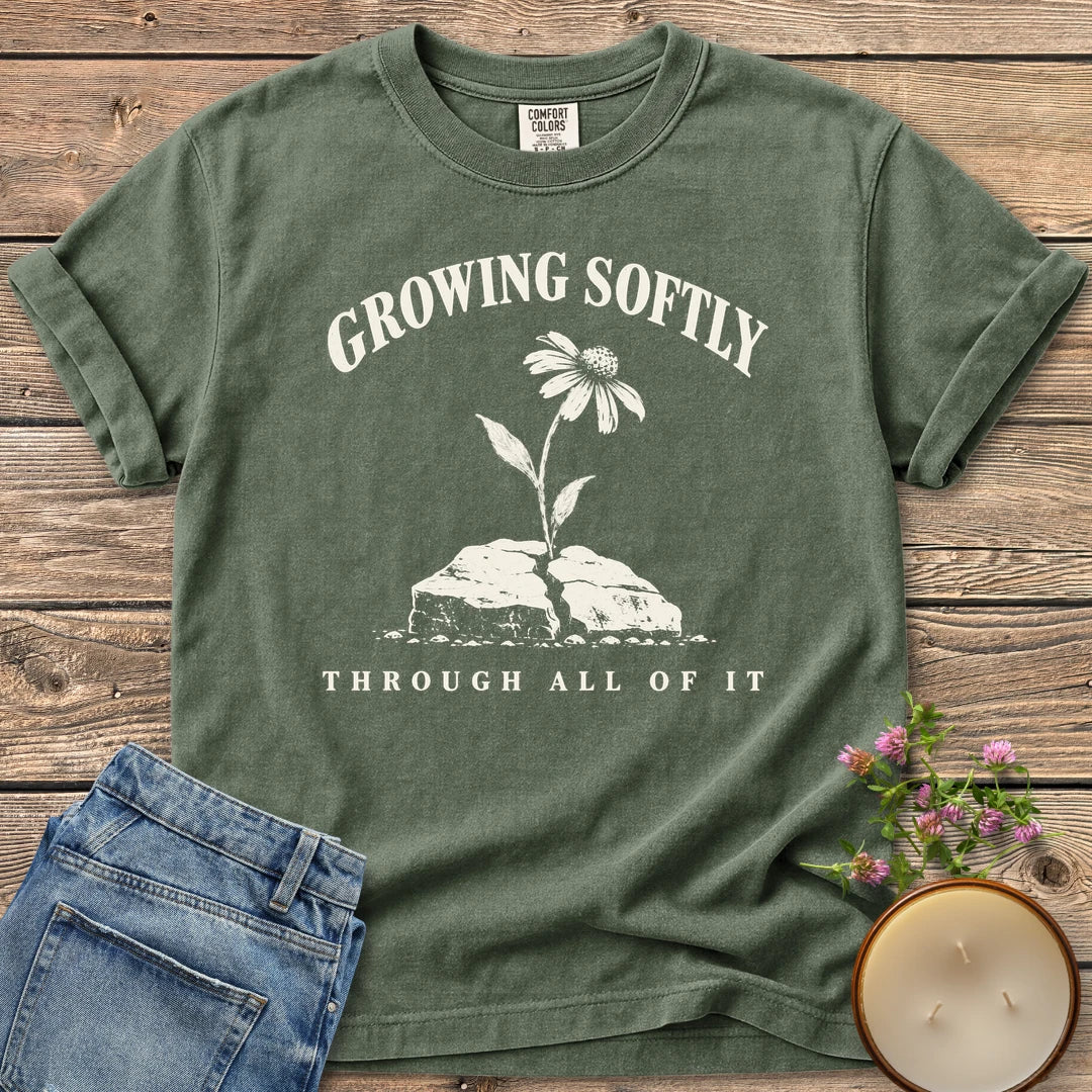 Growing Softly Through It All t-shirt, Growing Softly above a flower breaking through a cracked rock and Through All Of It, on a Moss Comfort Colors tee