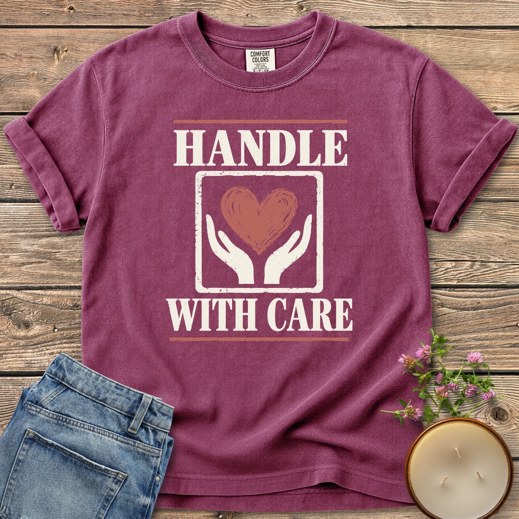 Handle With Care t-shirt, Handle With Care around two hands holding a heart, on a Berry Comfort Colors tee