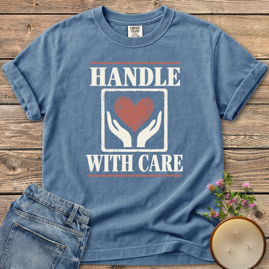 Handle With Care t-shirt, Handle With Care around two hands holding a heart, on a Blue Jean Comfort Colors tee