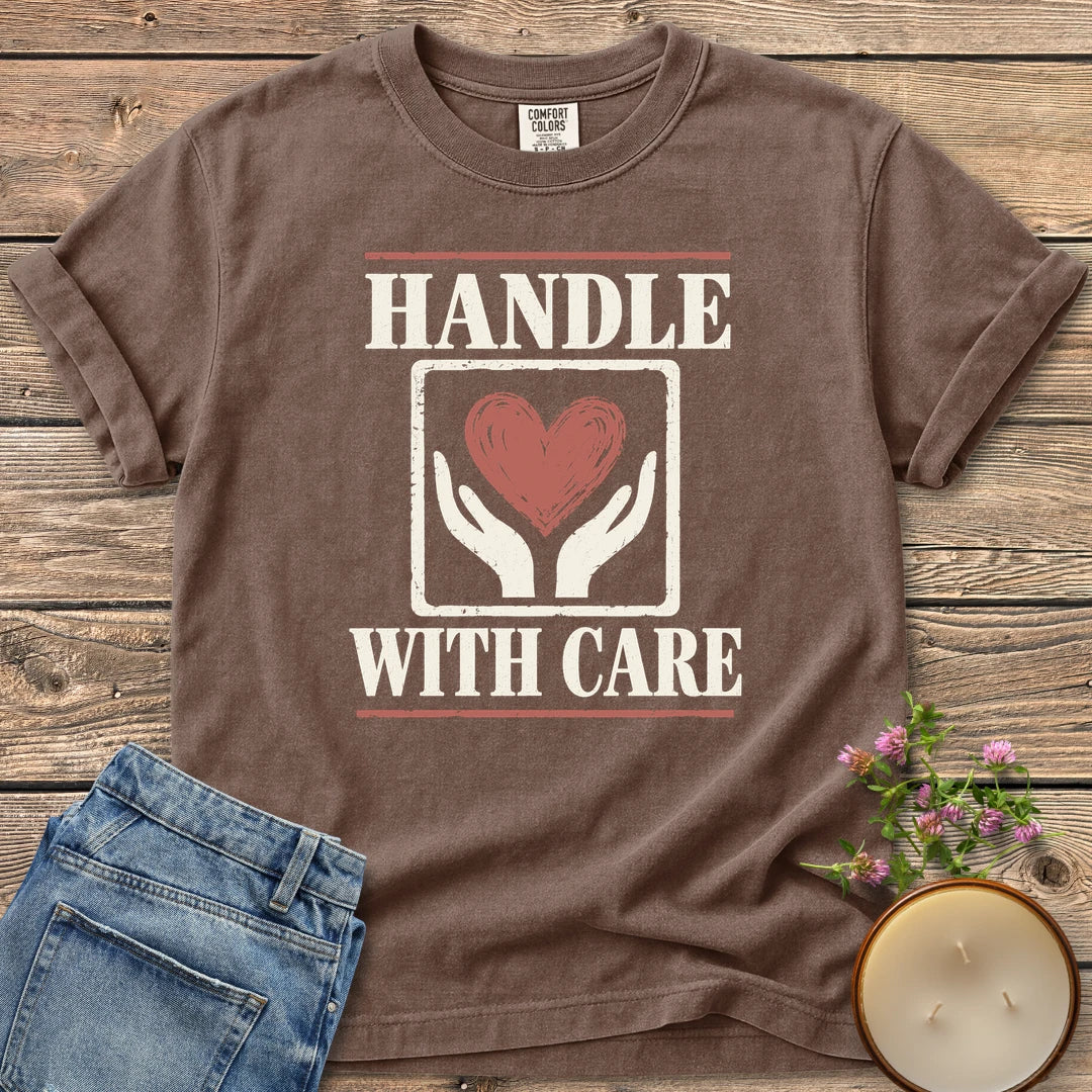 Handle With Care t-shirt, Handle With Care around two hands holding a heart, on an Espresso Comfort Colors tee