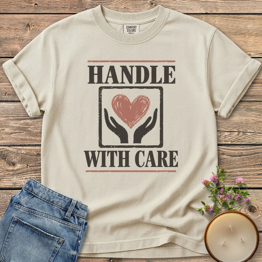 Handle With Care t-shirt, Handle With Care around two hands holding a heart, on an Ivory Comfort Colors tee