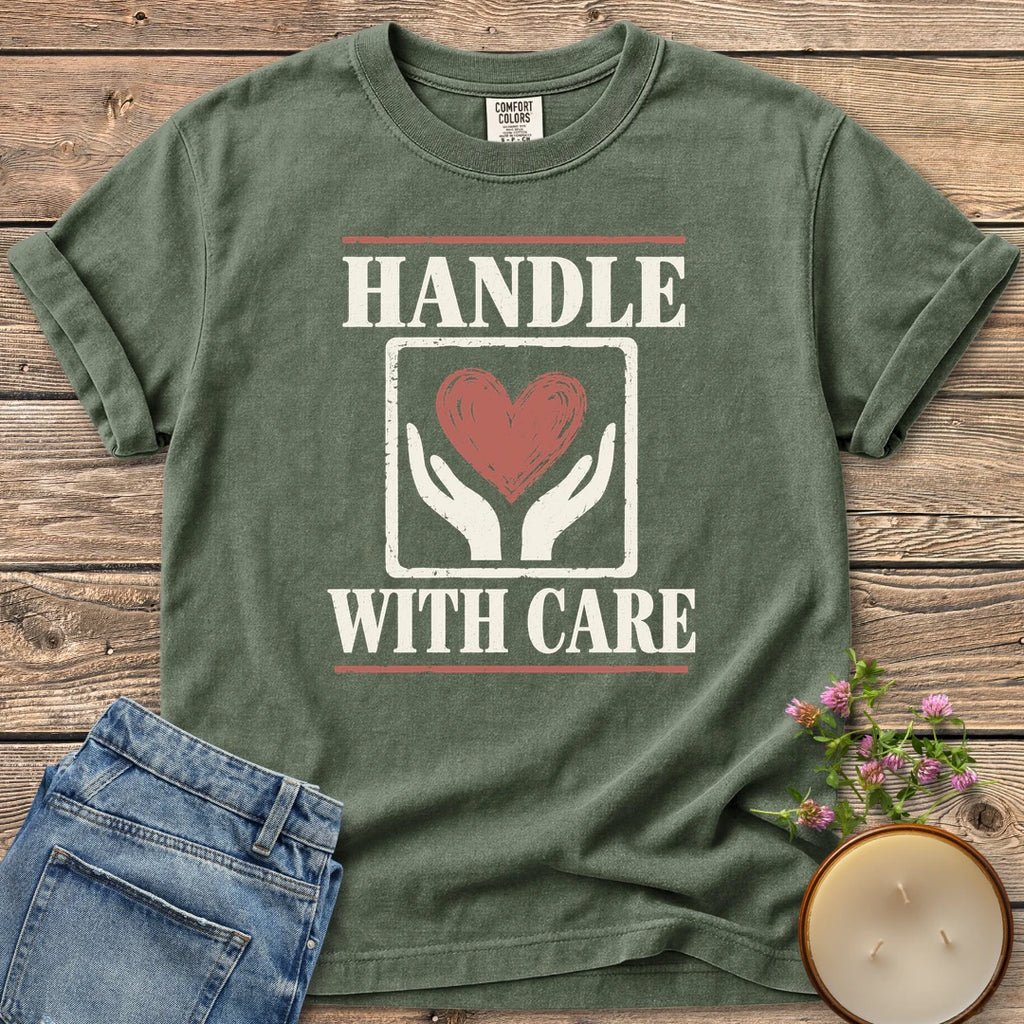 Handle With Care t-shirt, Handle With Care around two hands holding a heart, on a Moss Comfort Colors tee