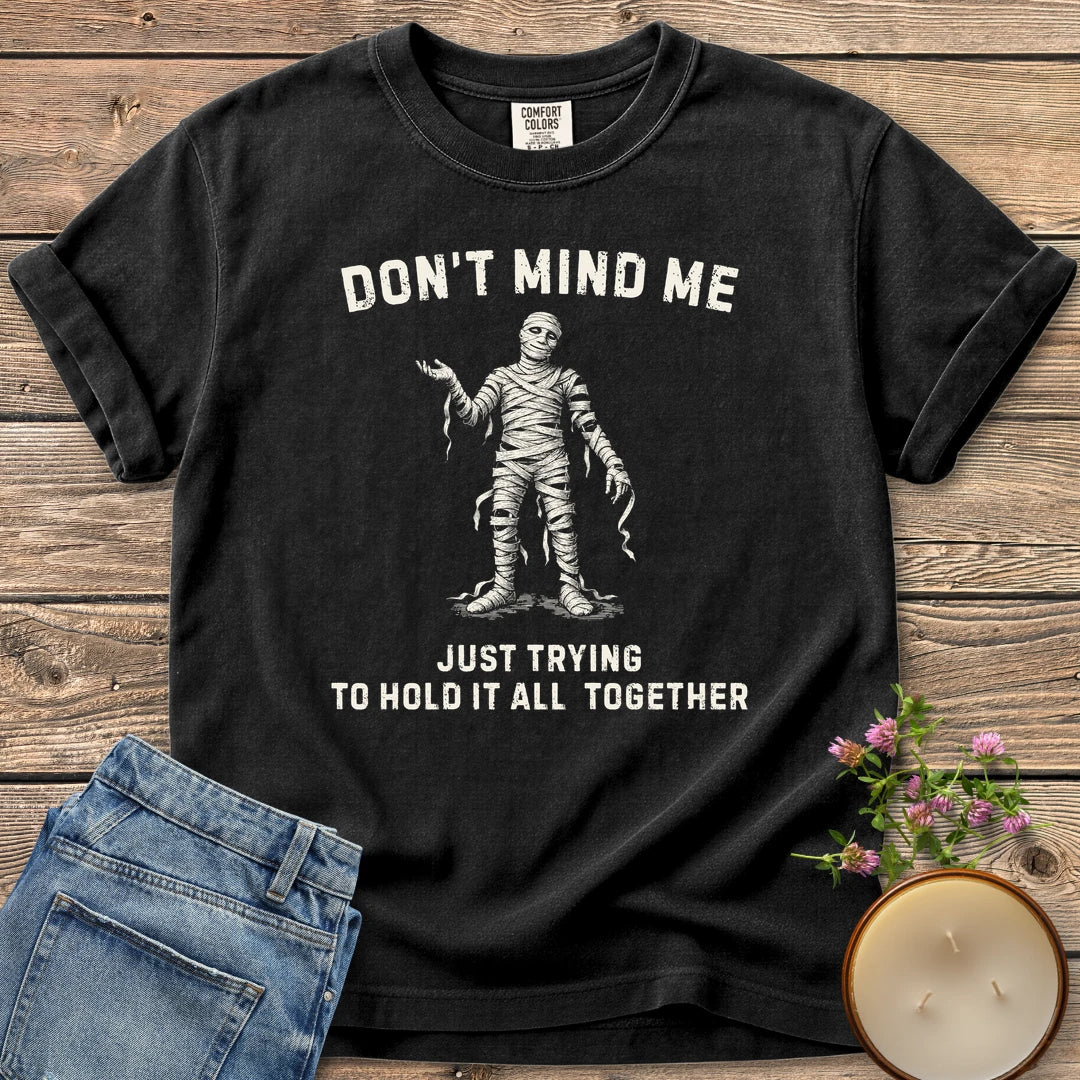 Hold It All Together t-shirt, a mummy with unraveling bandages between Don't Mind Me and Just Trying To Hold It All Together, on a Black Comfort Colors tee