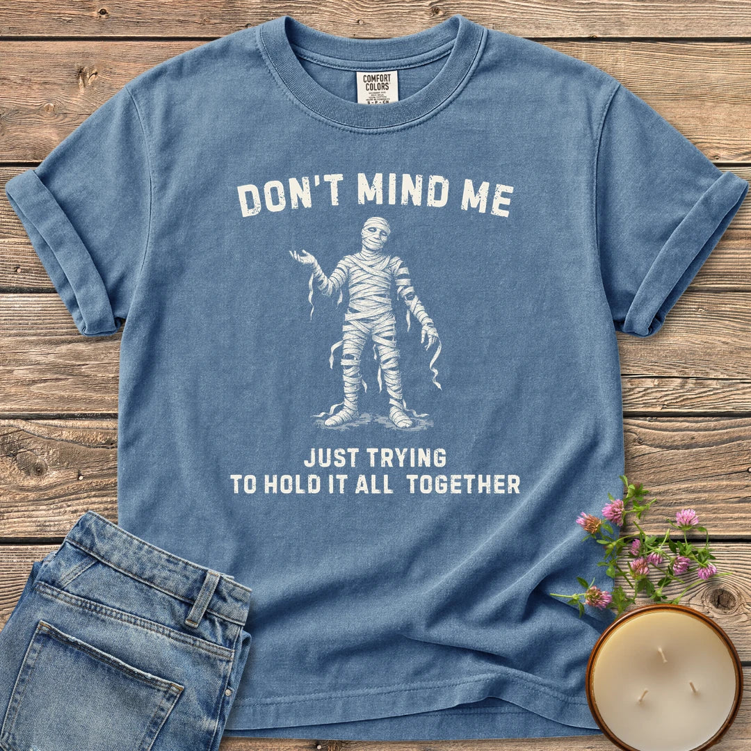 Hold It All Together t-shirt, a mummy with unraveling bandages between Don't Mind Me and Just Trying To Hold It All Together, on a Blue Jean Comfort Colors tee