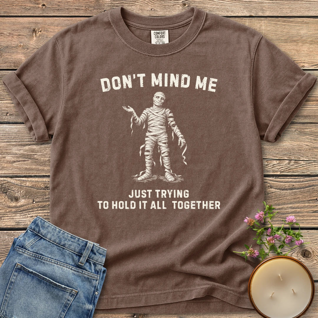 Hold It All Together t-shirt, a mummy with unraveling bandages between Don't Mind Me and Just Trying To Hold It All Together, on an Espresso Comfort Colors tee
