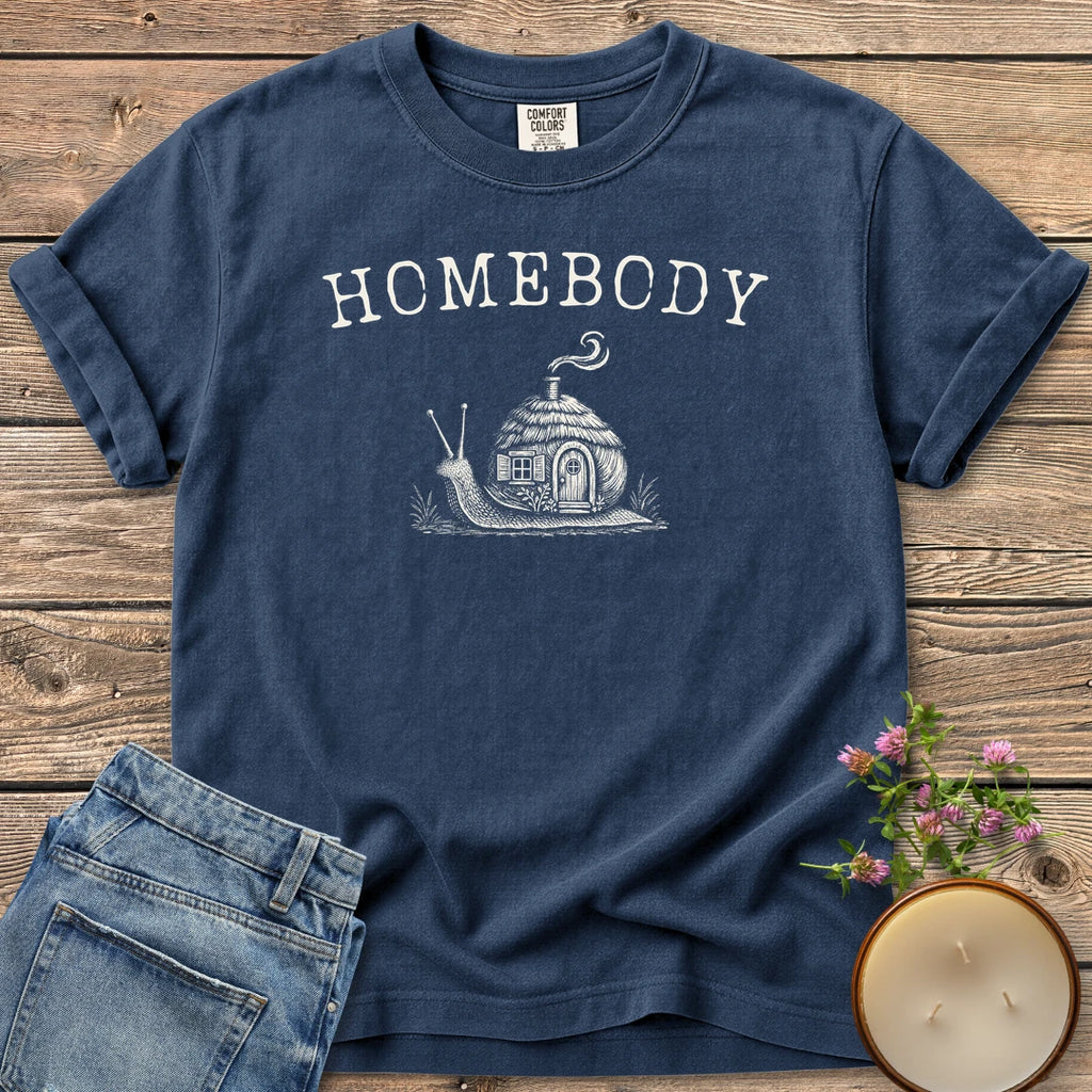 Homebody t-shirt, a snail carrying a tiny cottage with a smoking chimney under Homebody, on a Navy Comfort Colors tee