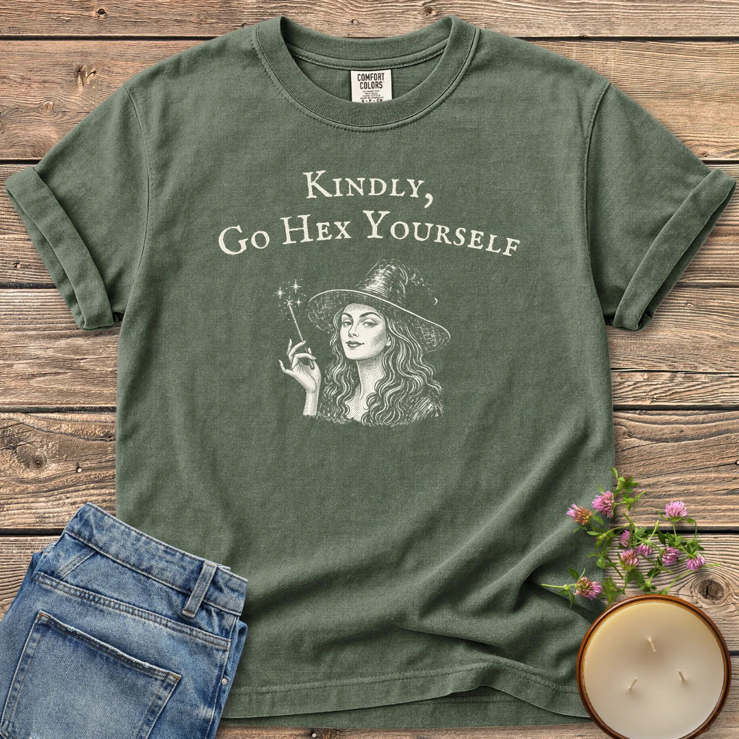 Kindly Go Hex Yourself t-shirt, a smiling witch with a wand under Kindly, Go Hex Yourself, on a Moss Comfort Colors tee