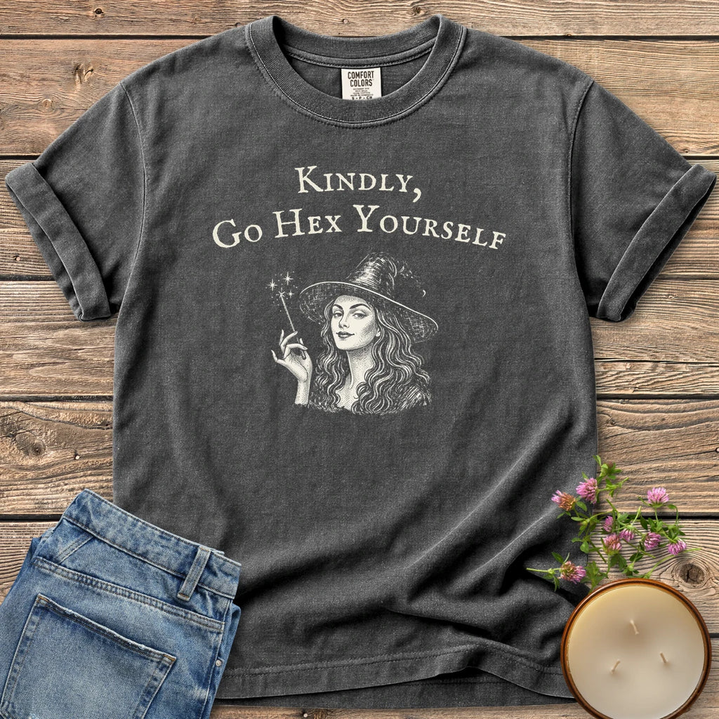 Kindly Go Hex Yourself t-shirt, a smiling witch with a wand under Kindly, Go Hex Yourself, on a Pepper Comfort Colors tee