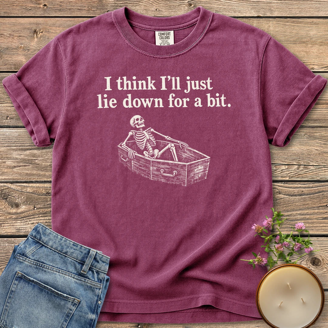 Lie Down For a Bit t-shirt, a skeleton lying in a coffin under I think I'll just lie down for a bit, on a Berry Comfort Colors tee