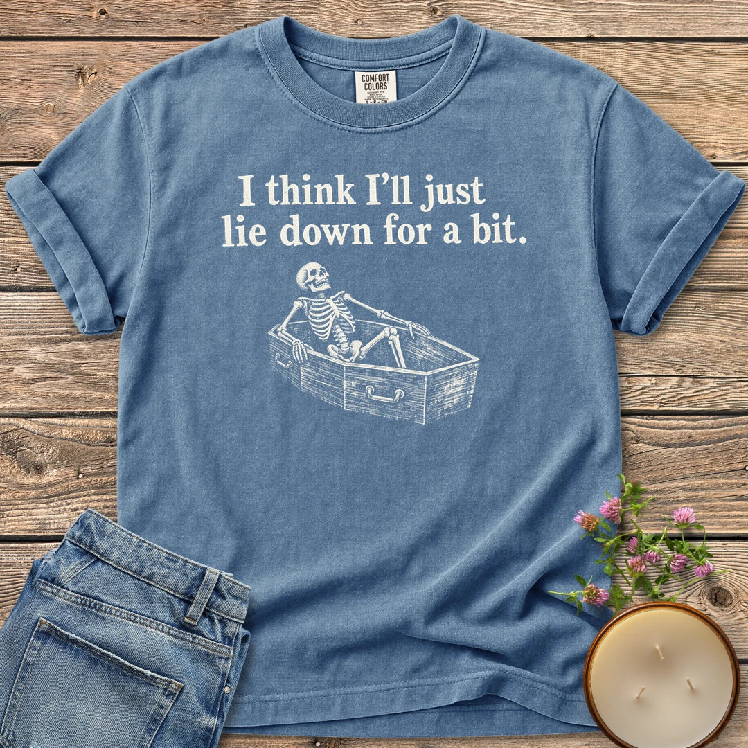 Lie Down For a Bit t-shirt, a skeleton lying in a coffin under I think I'll just lie down for a bit, on a Blue Jean Comfort Colors tee