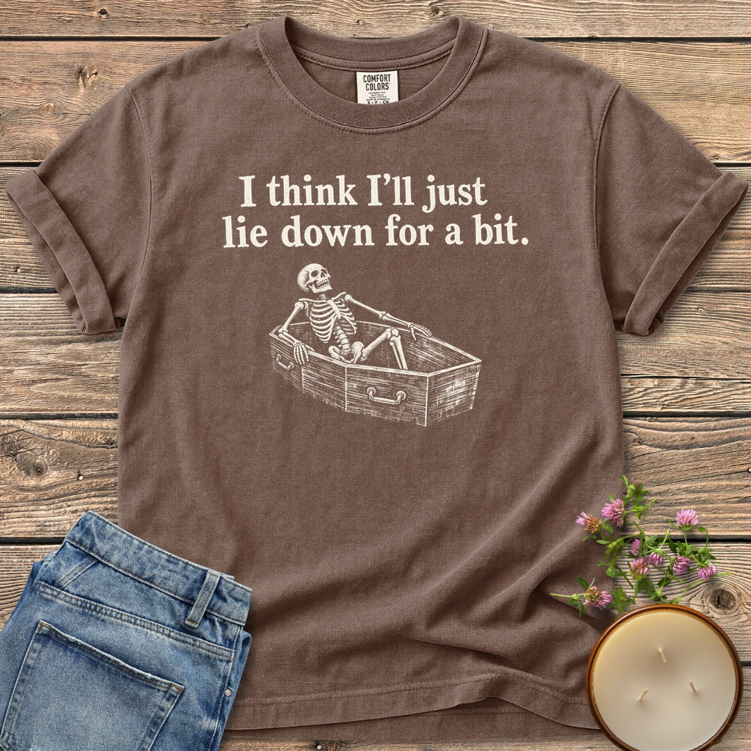 Lie Down For a Bit t-shirt, a skeleton lying in a coffin under I think I'll just lie down for a bit, on an Espresso Comfort Colors tee