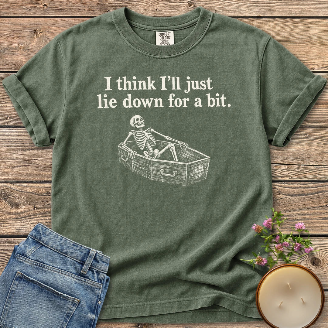 Lie Down For a Bit t-shirt, a skeleton lying in a coffin under I think I'll just lie down for a bit, on a Moss Comfort Colors tee