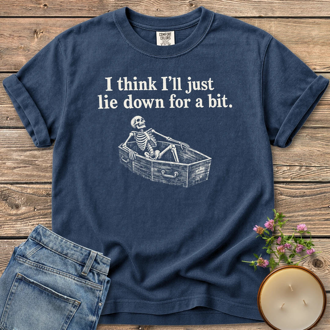 Lie Down For a Bit t-shirt, a skeleton lying in a coffin under I think I'll just lie down for a bit, on a Navy Comfort Colors tee