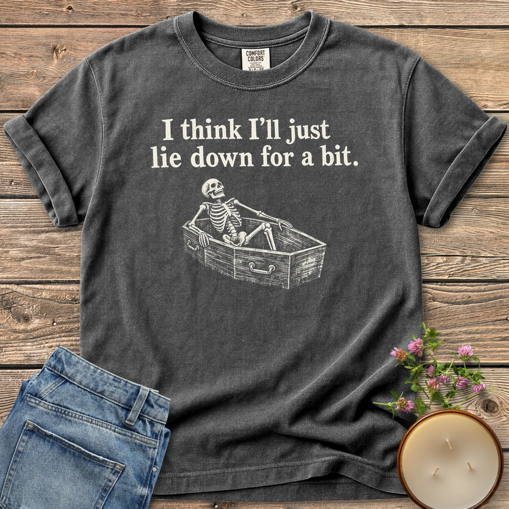 Lie Down For a Bit t-shirt, a skeleton lying in a coffin under I think I'll just lie down for a bit, on a Pepper Comfort Colors tee