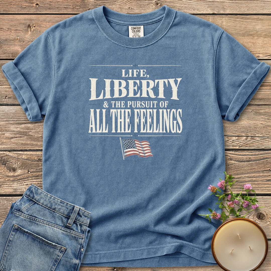Life Liberty All the Feelings t-shirt, Life, Liberty & The Pursuit of All The Feelings in vintage type with a waving American flag, on a Blue Jean Comfort Colors tee