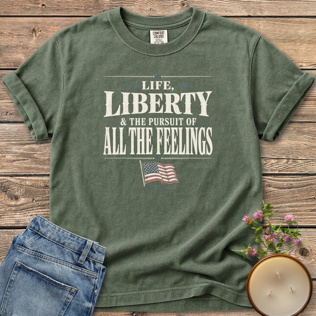Life Liberty All the Feelings t-shirt, Life, Liberty & The Pursuit of All The Feelings in vintage type with a waving American flag, on a Moss Comfort Colors tee