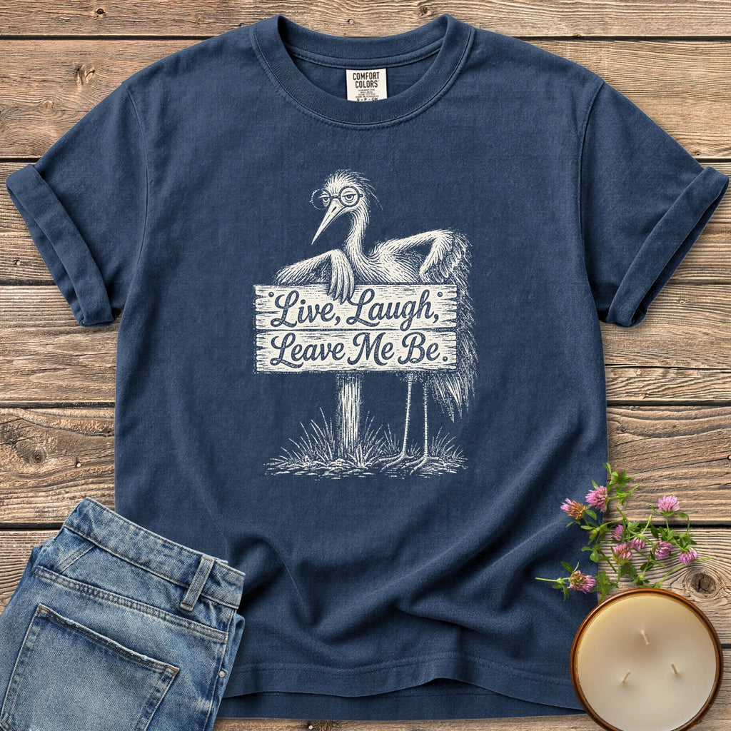 Live Laugh Leave Me Be t-shirt, a grumpy heron in glasses leaning on a sign that reads Live, Laugh, Leave Me Be, on a Navy Comfort Colors tee