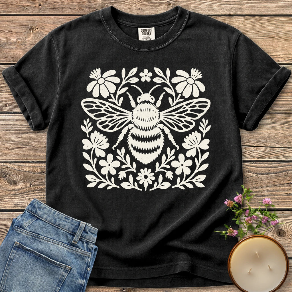 Meadow Bee Folk Art Flat t-shirt, a folk art bee surrounded by flat wildflowers, on a Black Comfort Colors tee