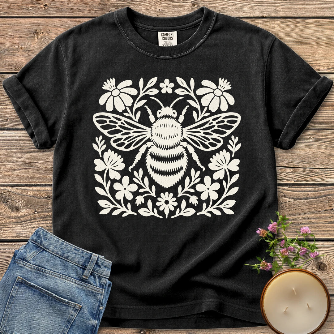 Meadow Bee Folk Art Flat t-shirt, a folk art bee surrounded by flat wildflowers, on a Black Comfort Colors tee
