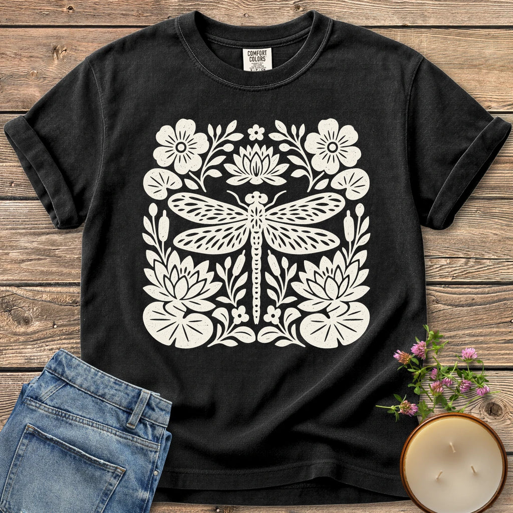 Meadow Dragonfly Folk Art Flat t-shirt, a folk art dragonfly surrounded by lily pads and flowers, on a Black Comfort Colors tee