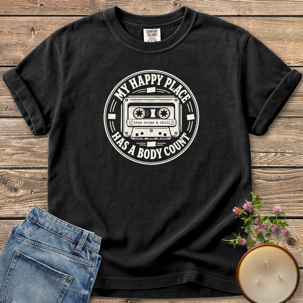 My Happy Place Body Count t-shirt, a round badge with a cassette tape reading My Happy Place Has A Body Count and true crime & chill, on a Black Comfort Colors tee