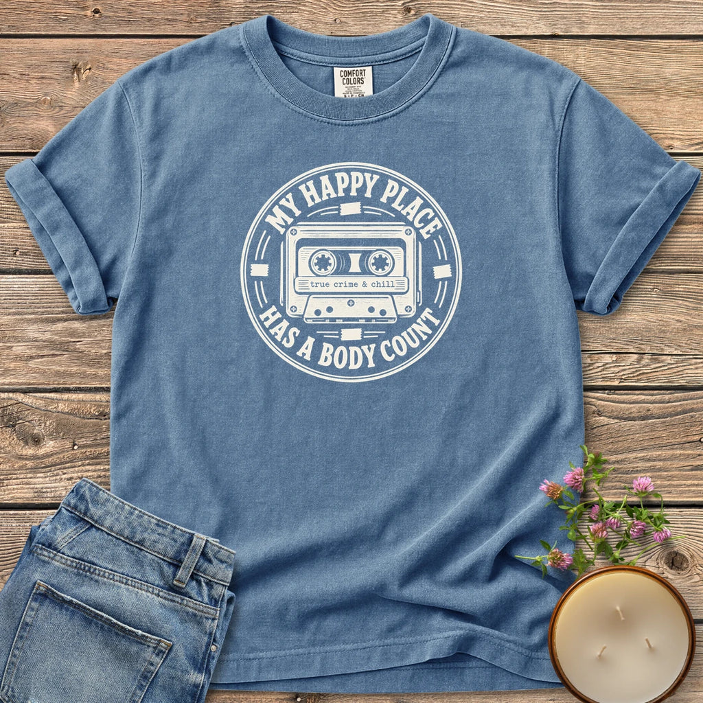 My Happy Place Body Count t-shirt, a round badge with a cassette tape reading My Happy Place Has A Body Count and true crime & chill, on a Blue Jean Comfort Colors tee