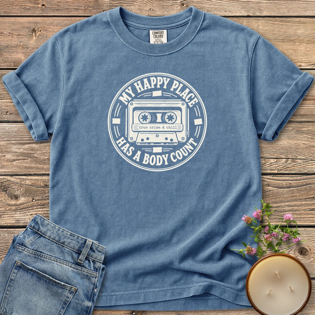 My Happy Place Body Count t-shirt, a round badge with a cassette tape reading My Happy Place Has A Body Count and true crime & chill, on a Blue Jean Comfort Colors tee