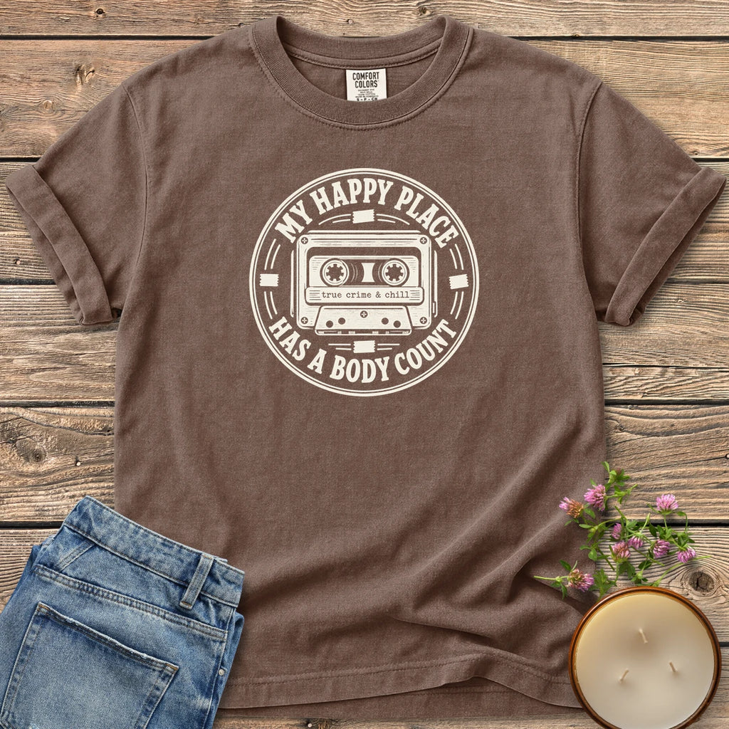 My Happy Place Body Count t-shirt, a round badge with a cassette tape reading My Happy Place Has A Body Count and true crime & chill, on an Espresso Comfort Colors tee