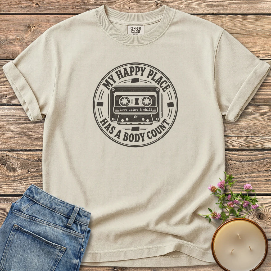 My Happy Place Body Count t-shirt, a round badge with a cassette tape reading My Happy Place Has A Body Count and true crime & chill, on an Ivory Comfort Colors tee