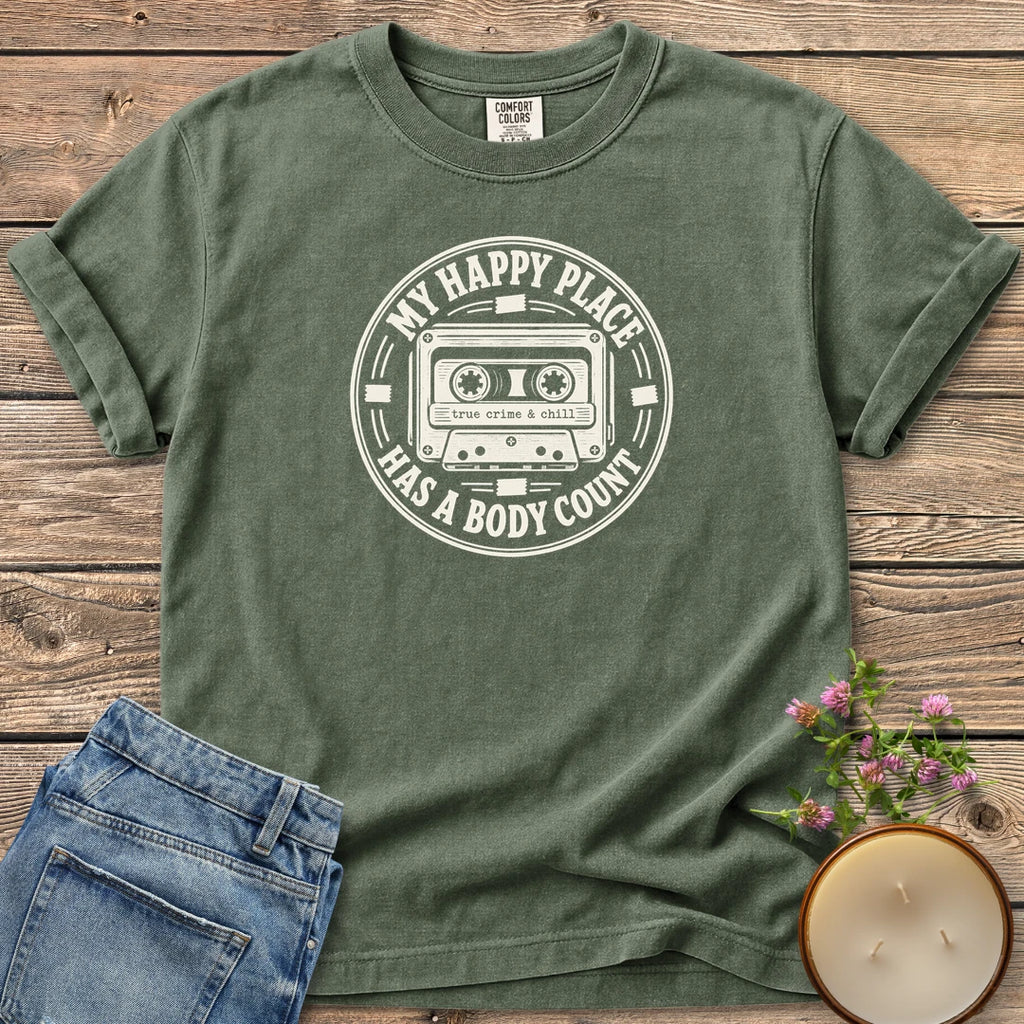 My Happy Place Body Count t-shirt, a round badge with a cassette tape reading My Happy Place Has A Body Count and true crime & chill, on a Moss Comfort Colors tee