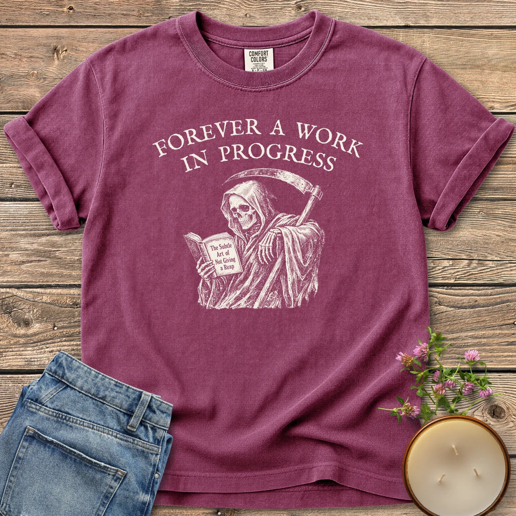 Not Giving A Reap t-shirt, a grim reaper reading The Subtle Art of Not Giving a Reap under Forever A Work In Progress, on a Berry Comfort Colors tee