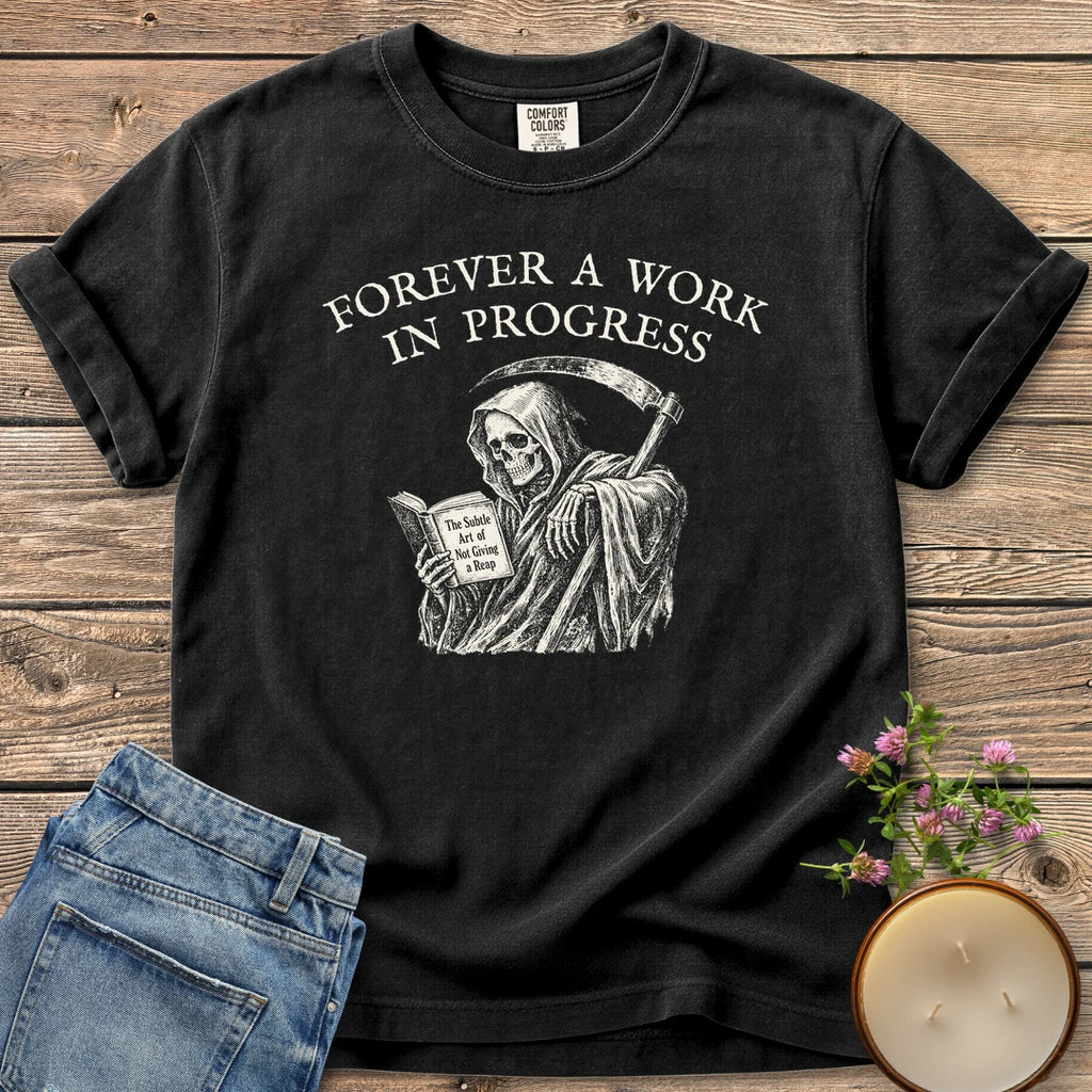 Not Giving A Reap t-shirt, a grim reaper reading The Subtle Art of Not Giving a Reap under Forever A Work In Progress, on a Black Comfort Colors tee