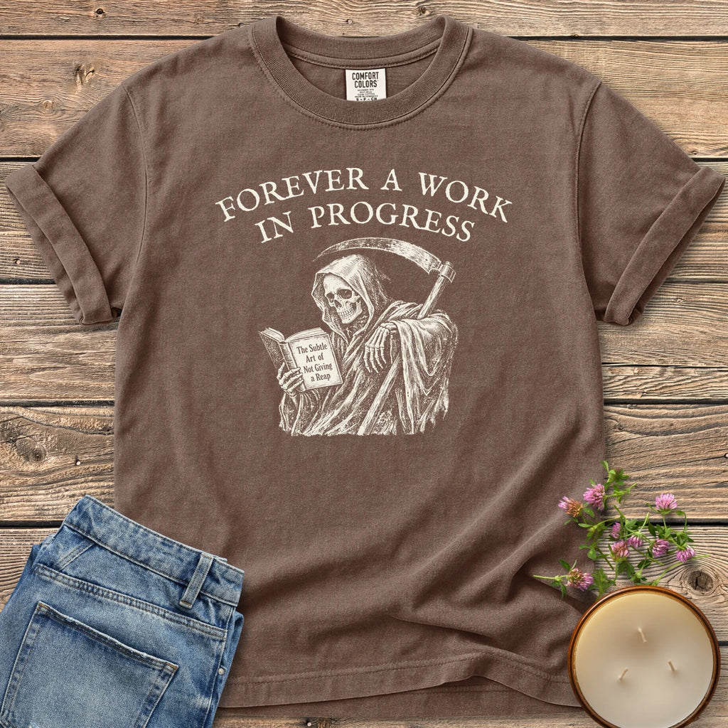 Not Giving A Reap t-shirt, a grim reaper reading The Subtle Art of Not Giving a Reap under Forever A Work In Progress, on an Espresso Comfort Colors tee