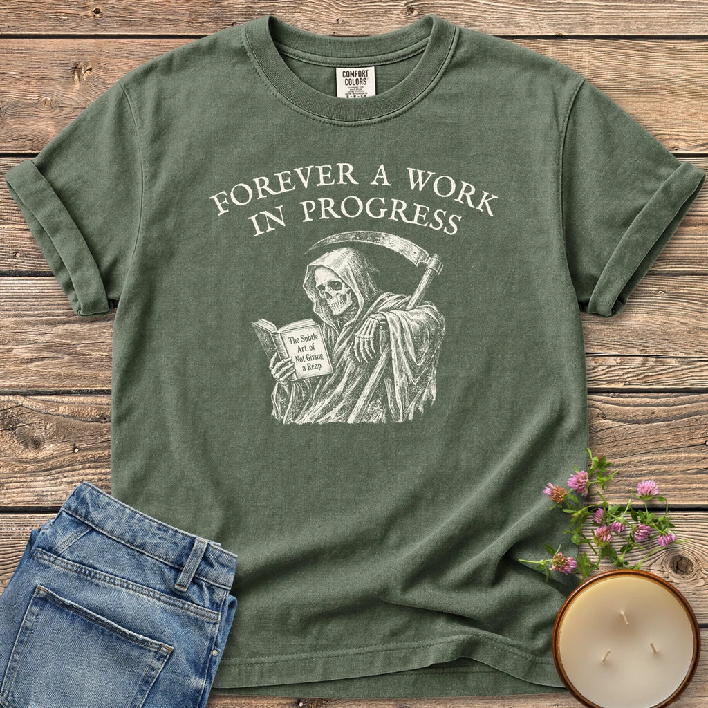Not Giving A Reap t-shirt, a grim reaper reading The Subtle Art of Not Giving a Reap under Forever A Work In Progress, on a Moss Comfort Colors tee