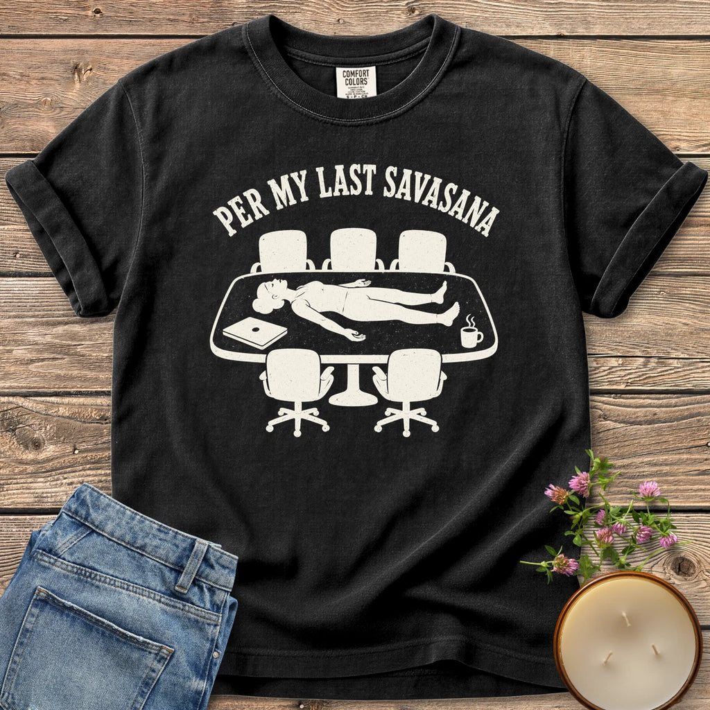 Per My Last Savasana t-shirt, a person lying flat on a conference table under Per My Last Savasana, on a Black Comfort Colors tee