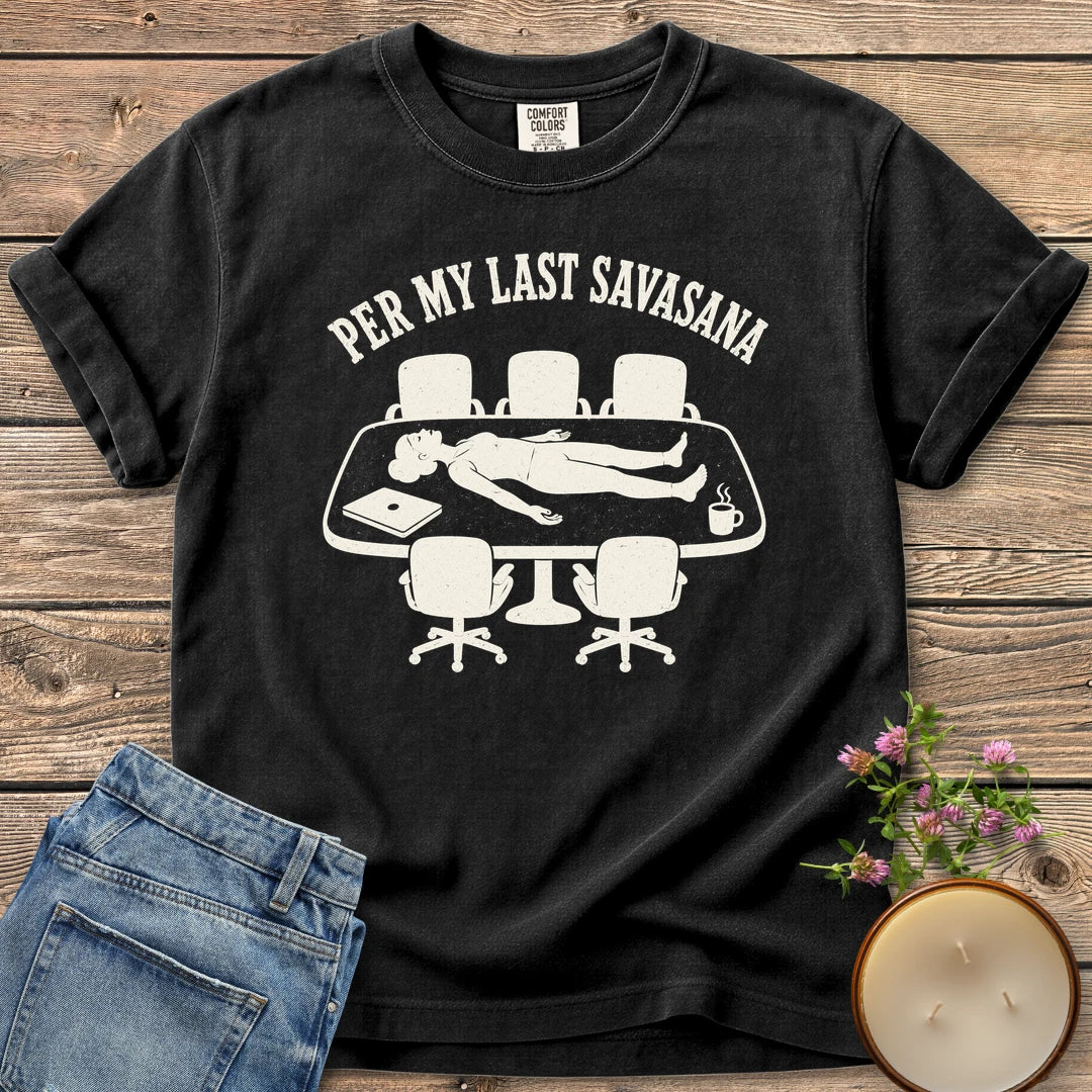 Per My Last Savasana t-shirt, a person lying flat on a conference table under Per My Last Savasana, on a Black Comfort Colors tee