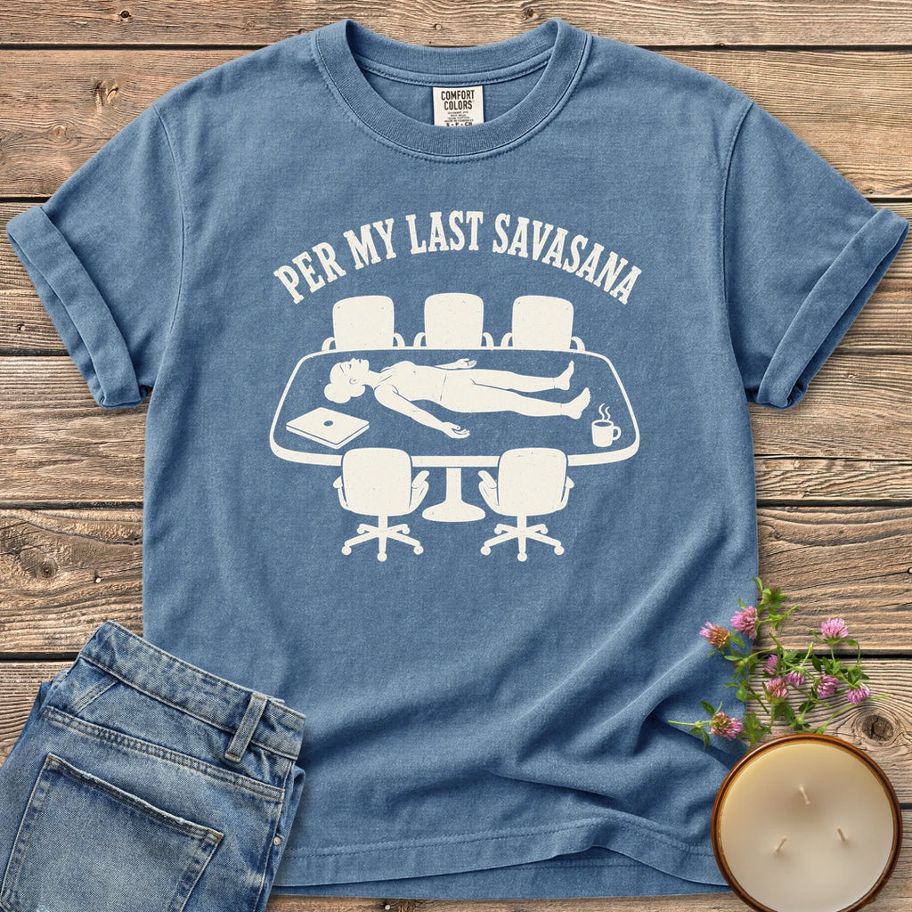 Per My Last Savasana t-shirt, a person lying flat on a conference table under Per My Last Savasana, on a Blue Jean Comfort Colors tee