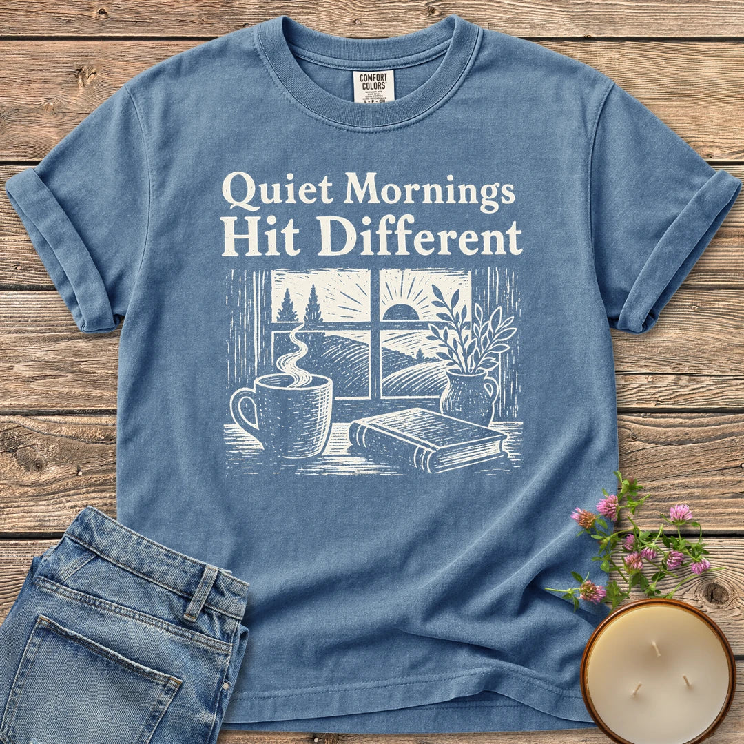 Quiet Mornings Hit Different t-shirt, Quiet Mornings Hit Different over a woodcut of coffee, a book and a window at sunrise, on a Blue Jean Comfort Colors tee