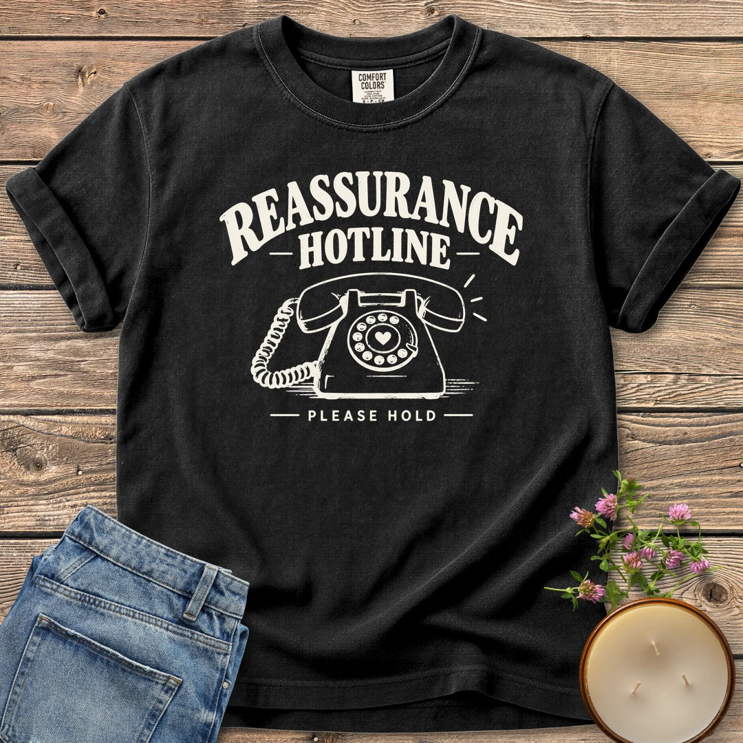 Reassurance Hotline Please Hold t-shirt, Reassurance Hotline above a rotary phone with a heart dial and Please Hold, on a Black Comfort Colors tee