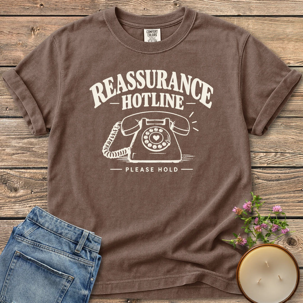 Reassurance Hotline Please Hold t-shirt, Reassurance Hotline above a rotary phone with a heart dial and Please Hold, on an Espresso Comfort Colors tee