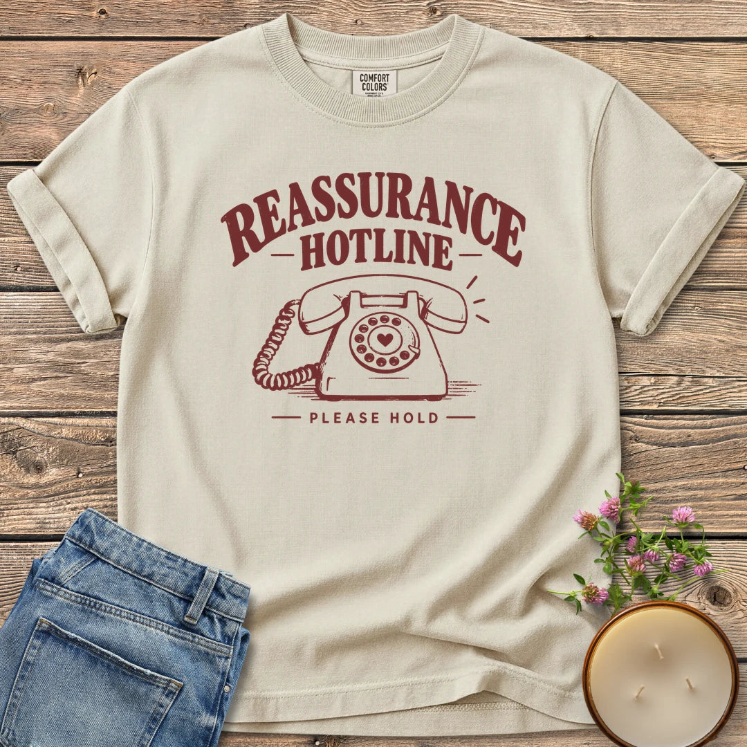 Reassurance Hotline Please Hold t-shirt, Reassurance Hotline above a rotary phone with a heart dial and Please Hold, on an Ivory Comfort Colors tee