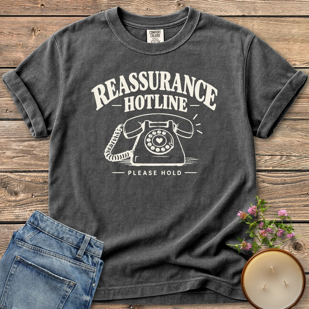 Reassurance Hotline Please Hold t-shirt, Reassurance Hotline above a rotary phone with a heart dial and Please Hold, on a Pepper Comfort Colors tee