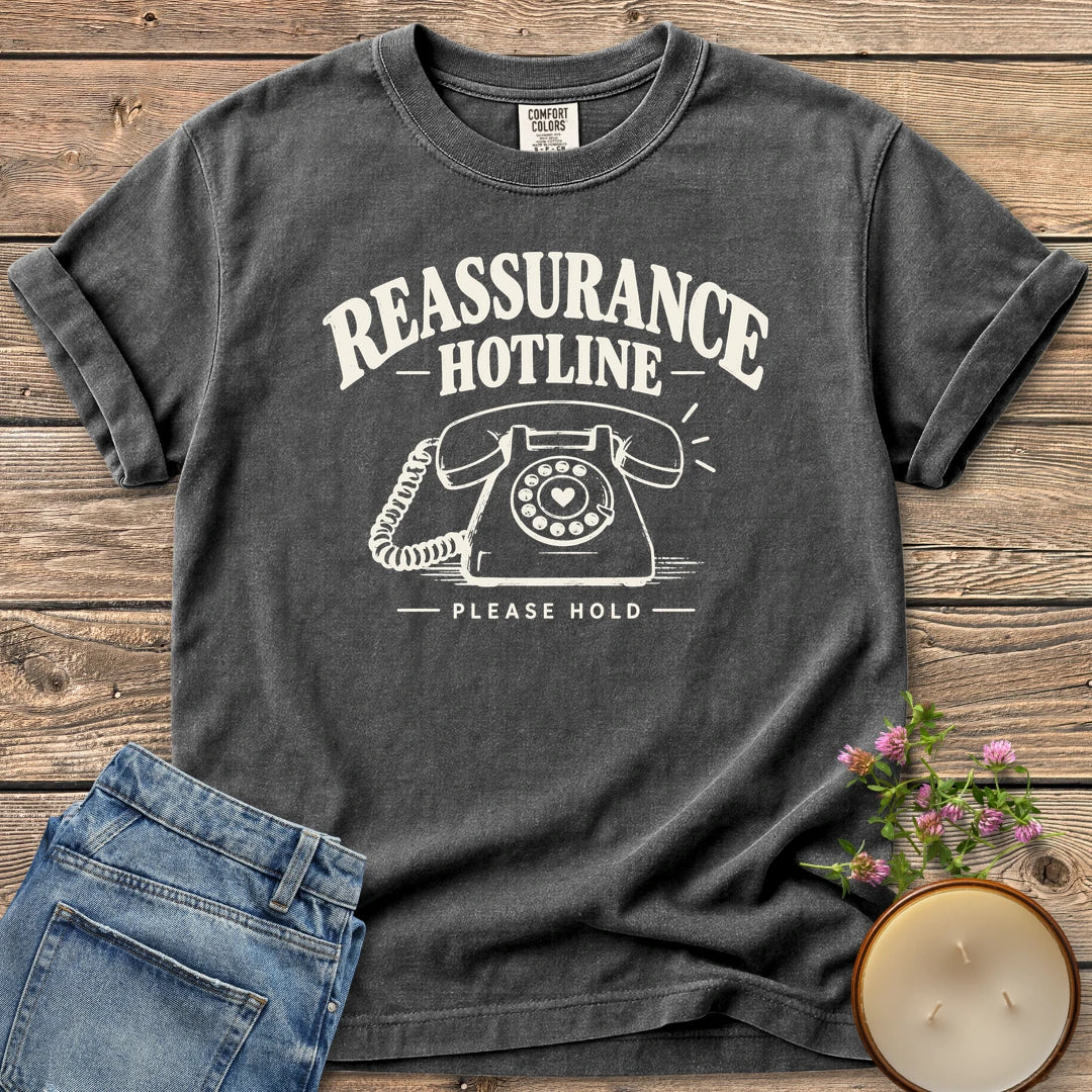 Reassurance Hotline Please Hold t-shirt, Reassurance Hotline above a rotary phone with a heart dial and Please Hold, on a Pepper Comfort Colors tee